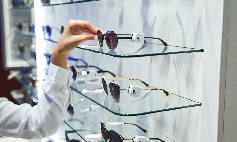 Female hand taking sunglasses from glass shelf in optical shop